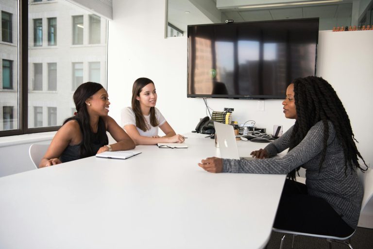 Three women collaborate in a modern office setting, discussing business plans and teamwork.